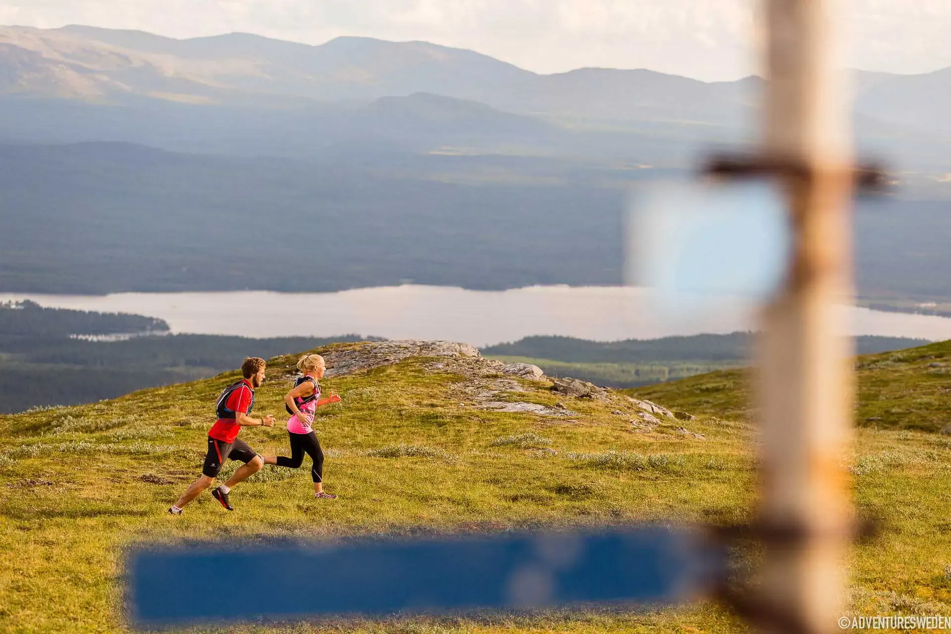 Två löpare på en bergsled med en sjö i bakgrunden.