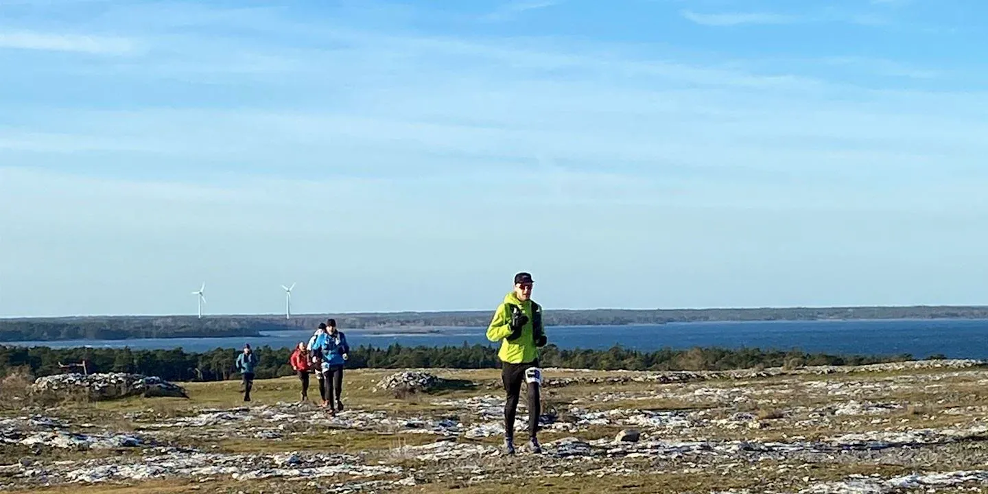 Löpare på en stig med utsikt över havet och vindkraftverk.