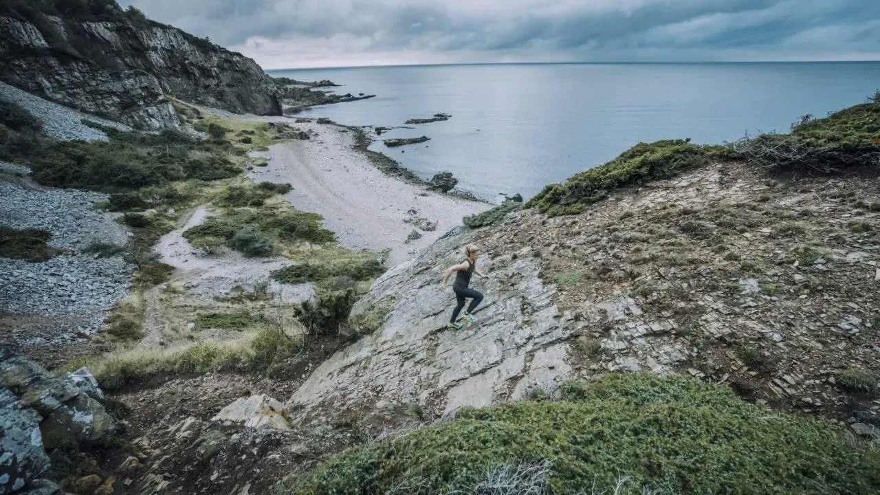 En löpare springer på en stenig kuststig med havet i bakgrunden.