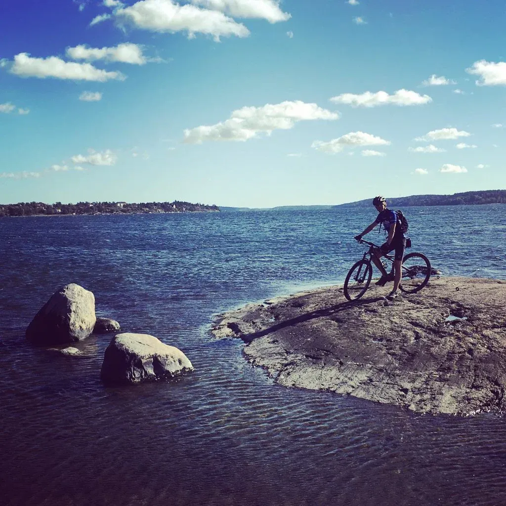 En person cyklar på en stenig kustlinje vid en sjö.