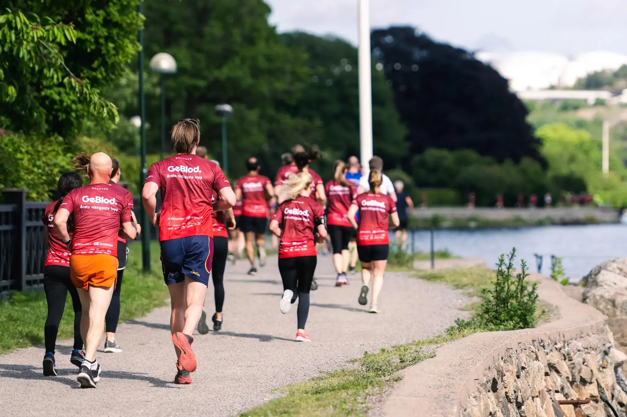 Löpare i röda tröjor springer vid vattnet. STHLM 10.